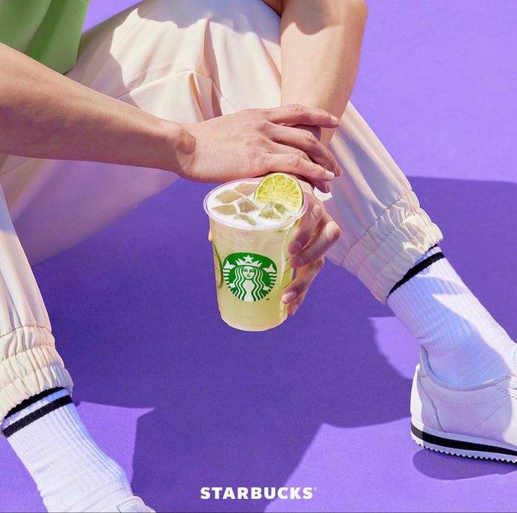 a person sitting on the ground holding a starbucks drink