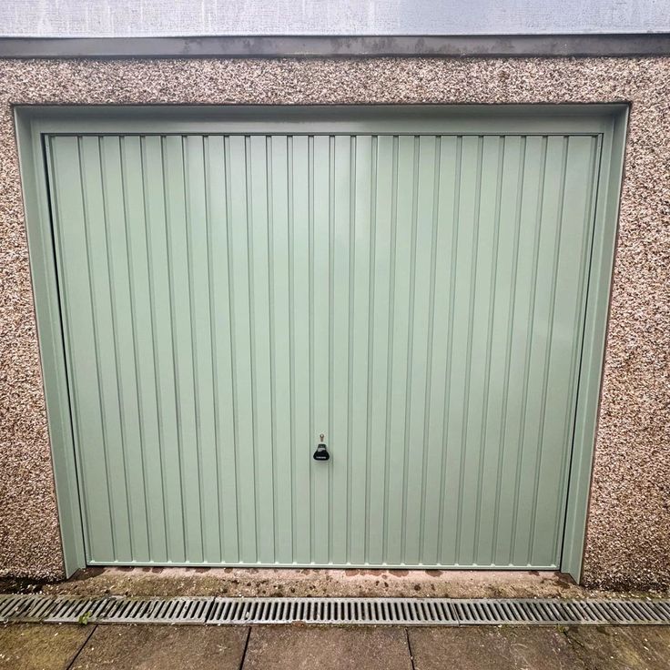 a green garage door with a grate on the ground next to it's side