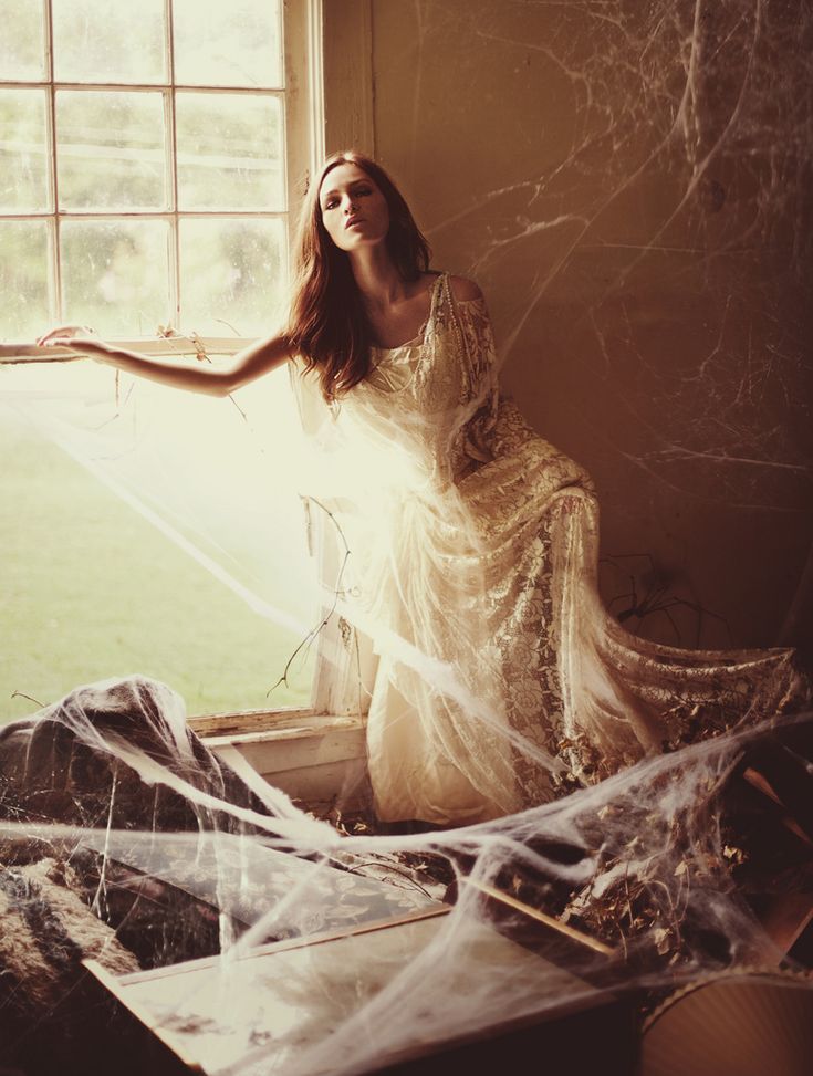 a woman sitting on the floor in front of a window wearing a white dress and veil