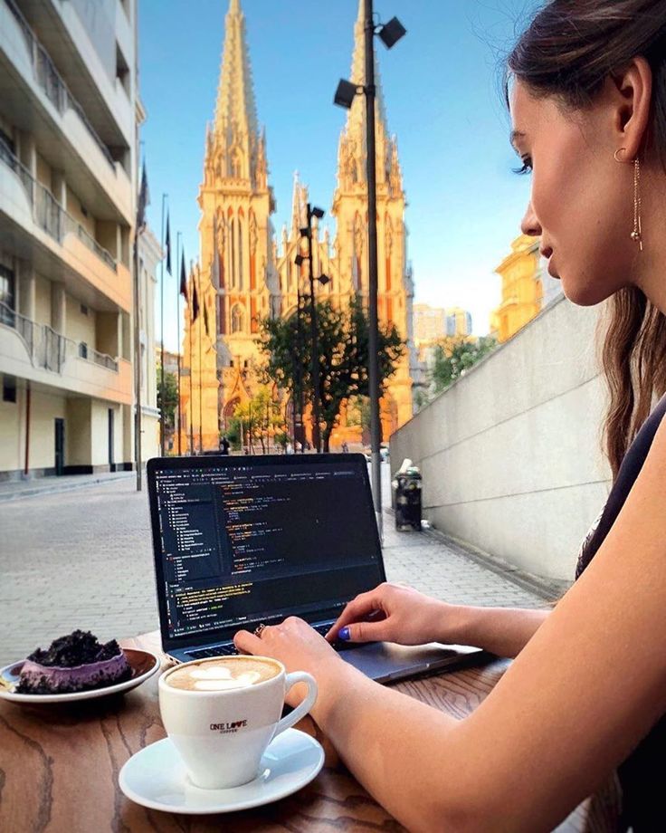 a woman sitting at a table with a laptop and cup of coffee in front of her