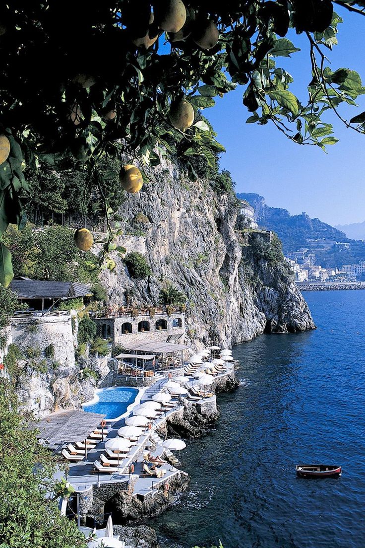 an outdoor swimming area with chaise lounges and fruit trees on the cliff side