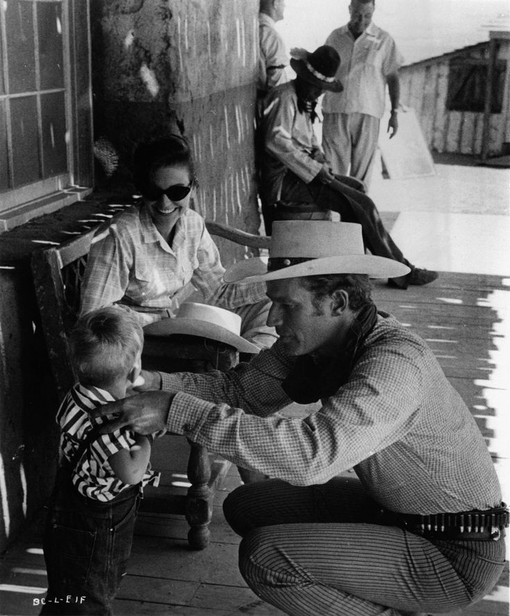 an old black and white photo of a man holding a baby in his lap with other people around him