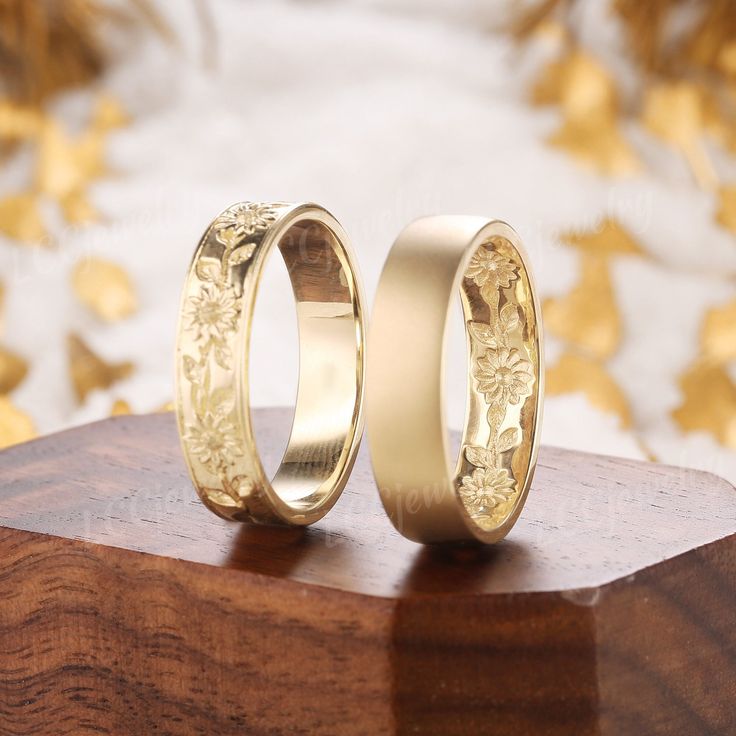 two gold wedding rings sitting on top of a wooden stand next to eachother