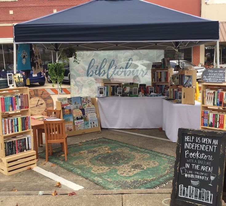 an outdoor book market with tables and chairs under a blue tent on the side walk