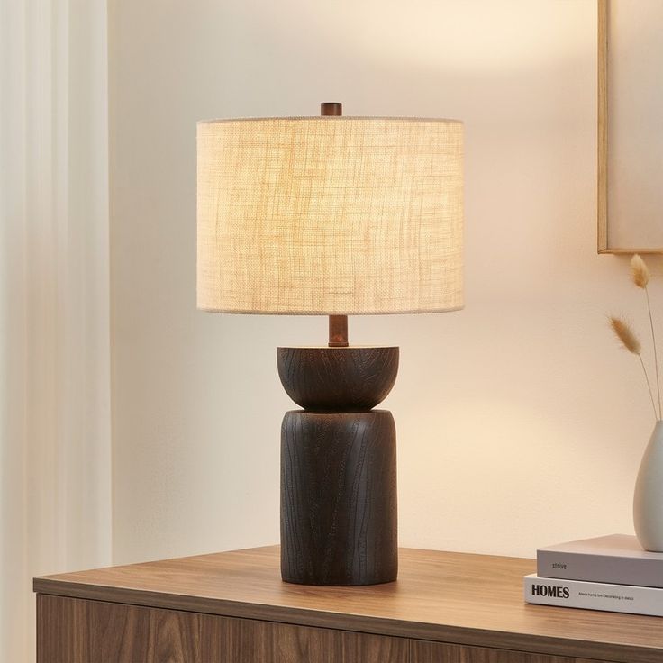 a table lamp sitting on top of a wooden dresser next to a book and vase