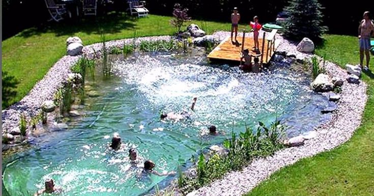 several people are playing in the water at a swimming pool that is surrounded by rocks and grass