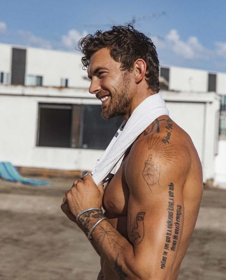 a shirtless man with tattoos on his arm and chest standing in front of a building