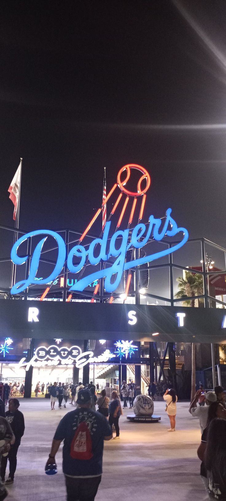 people are walking around in front of dodger's sign at night with the lights on