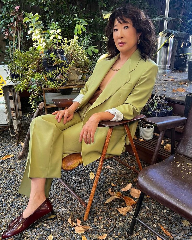 a woman sitting in a chair with her legs crossed and wearing a green suit on