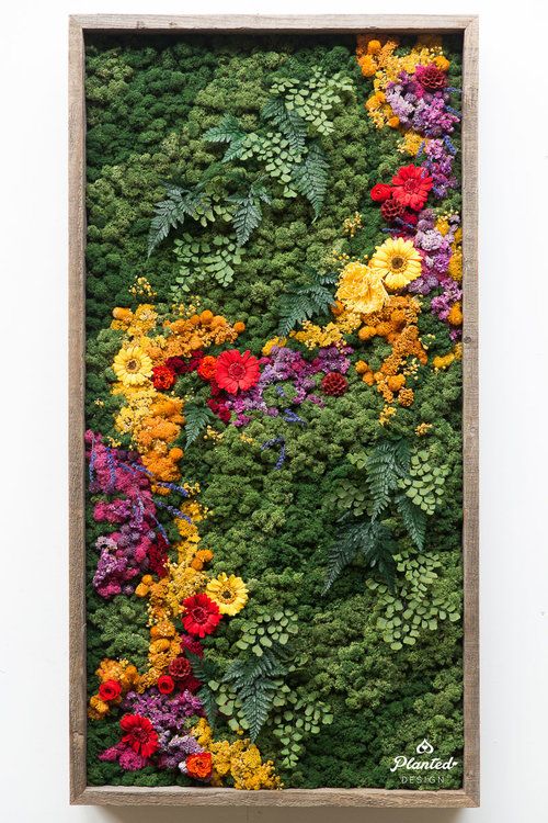 an arrangement of colorful flowers in a wooden frame on the side of a white wall