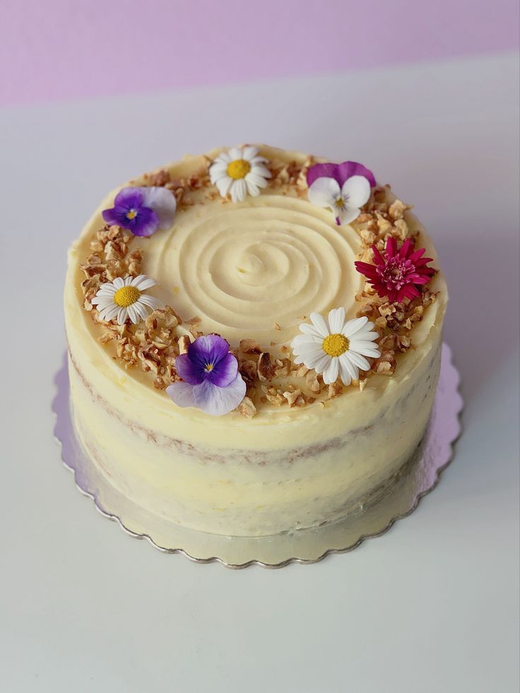 a white cake with flowers on it sitting on a table next to a pink wall