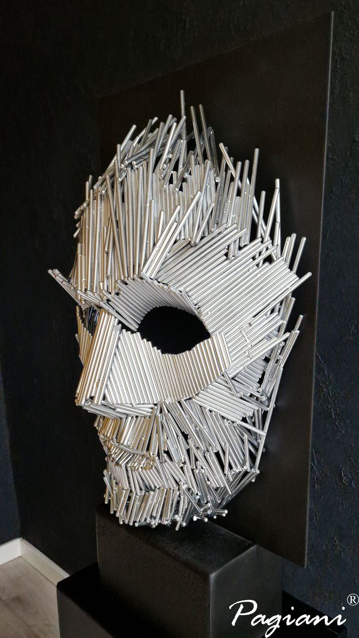 a sculpture made out of sticks on top of a black stand in front of a wall