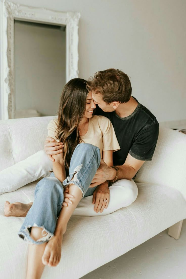 a man and woman sitting on top of a white couch next to each other in front of a mirror