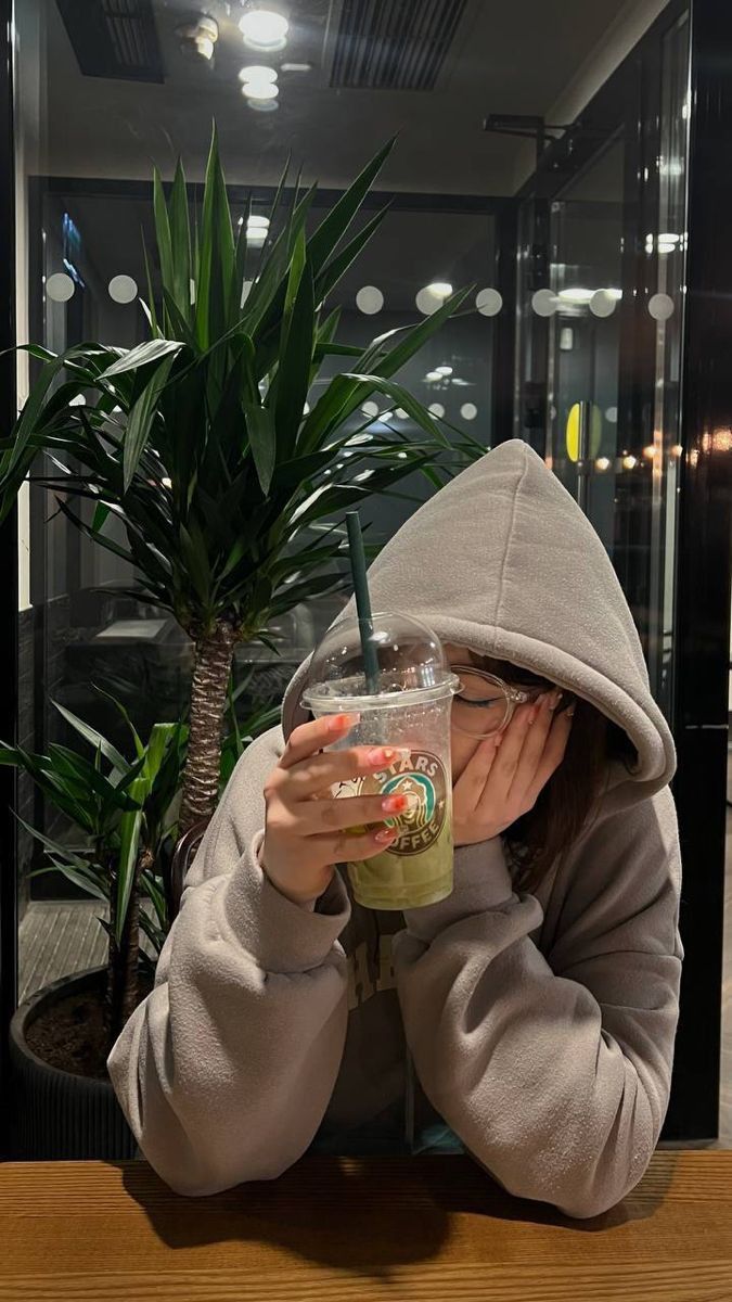 a person sitting at a table with a drink in front of their face, covering her eyes