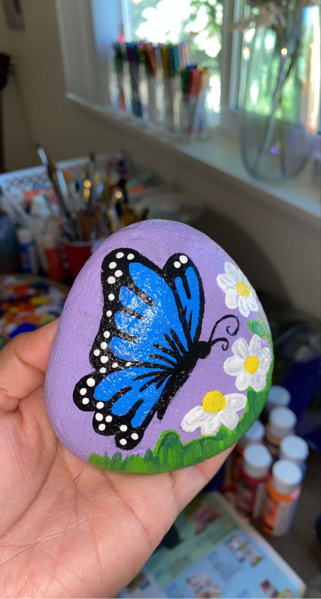 a hand holding a painted rock with a butterfly on it