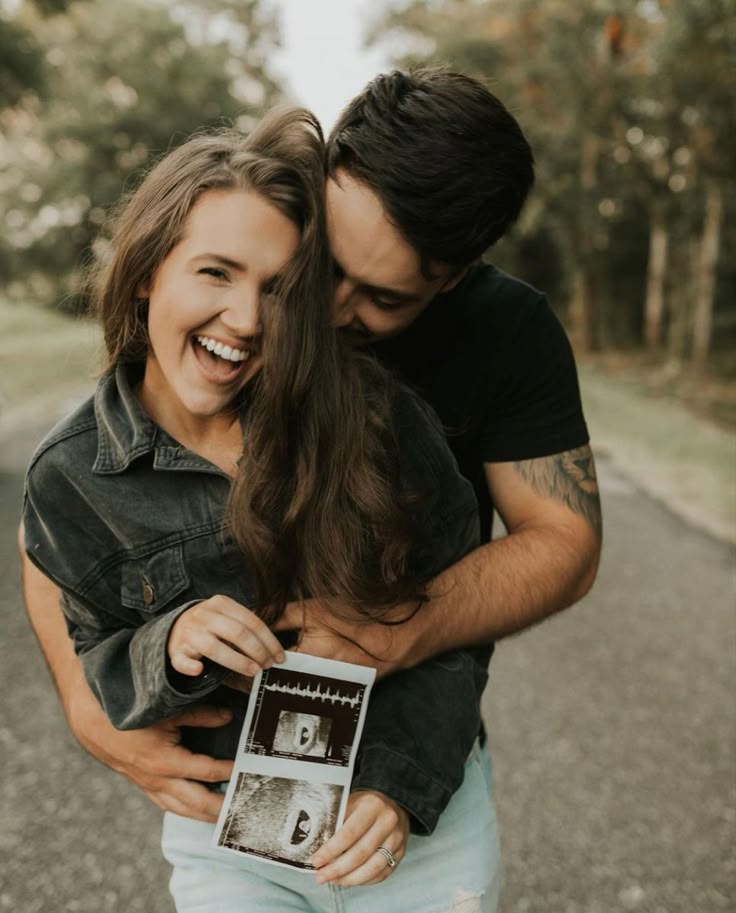 a man holding a woman in his arms and smiling at the camera while she holds an old photo