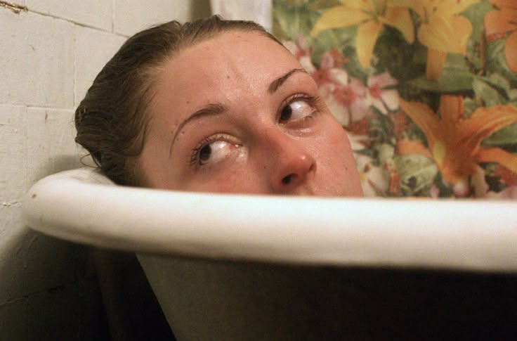 a woman looks up from behind a bathtub