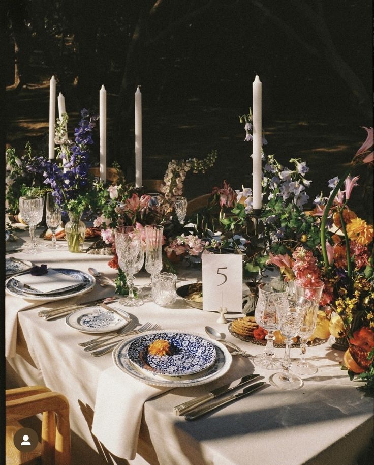 the table is set with flowers and candles for an outdoor dinner party or gathering in the garden