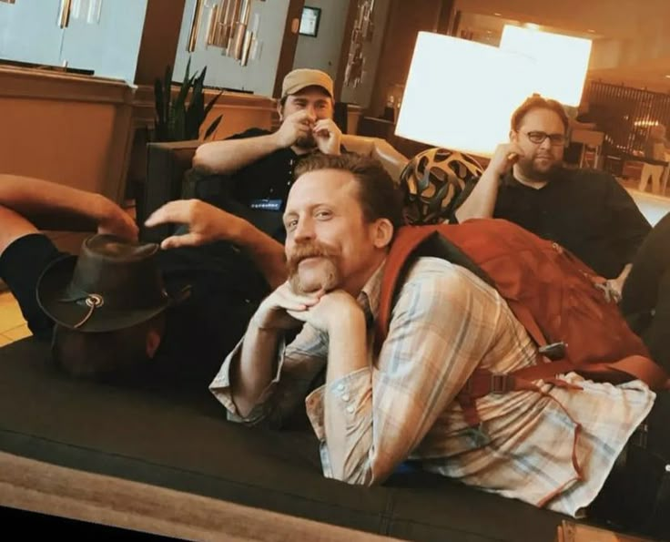 four men are sitting on the floor in a hotel lobby and one is holding a hat