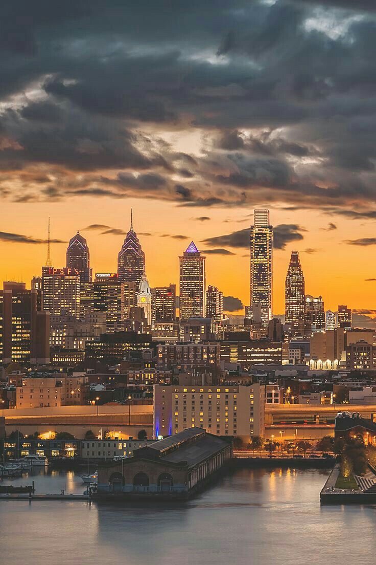 the city skyline is lit up at night as seen from across the water with clouds in the sky