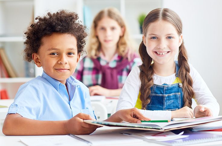 two young children sitting at a table with books and notebooks on top of them