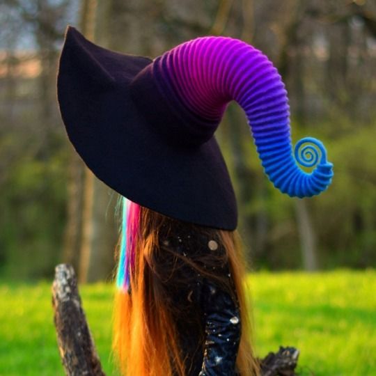 a woman with long hair wearing a black hat and rainbow colored wig sitting on a tree branch