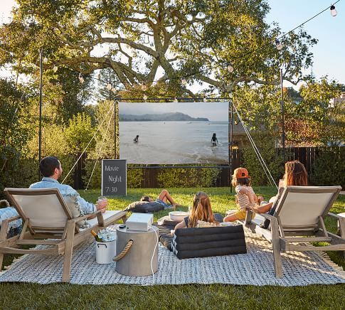 a group of people sitting on top of a blanket in front of a movie screen