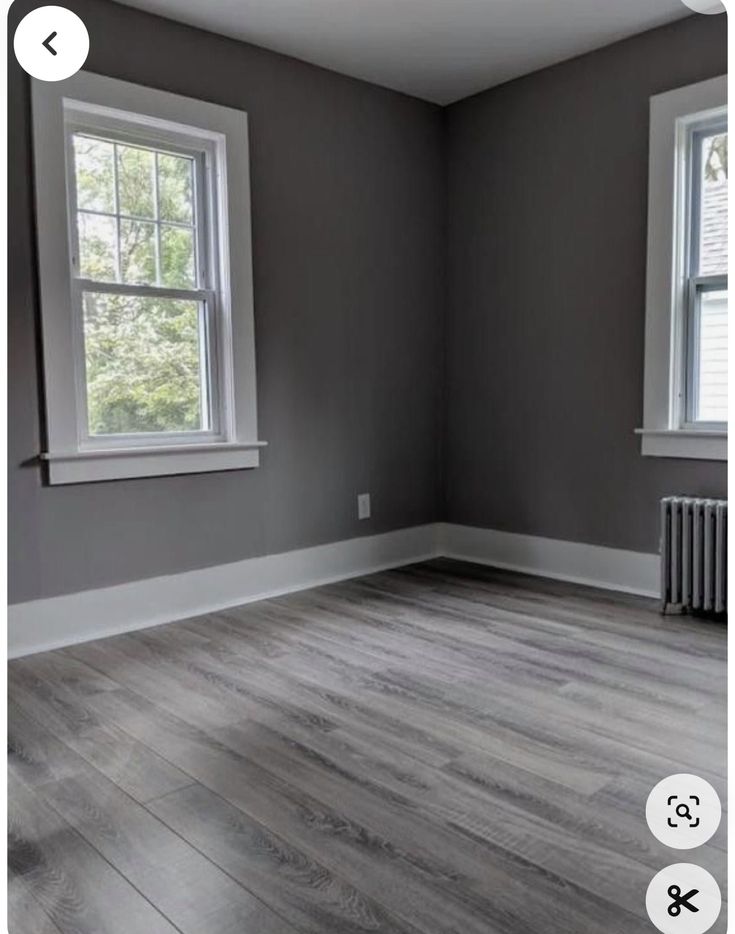 an empty room with wood floors and two windows in the corner, one is painted gray