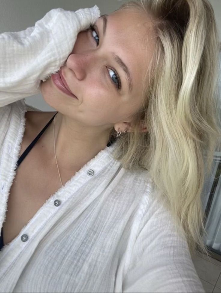 a woman with blonde hair wearing a white shirt and black necklace looking at the camera