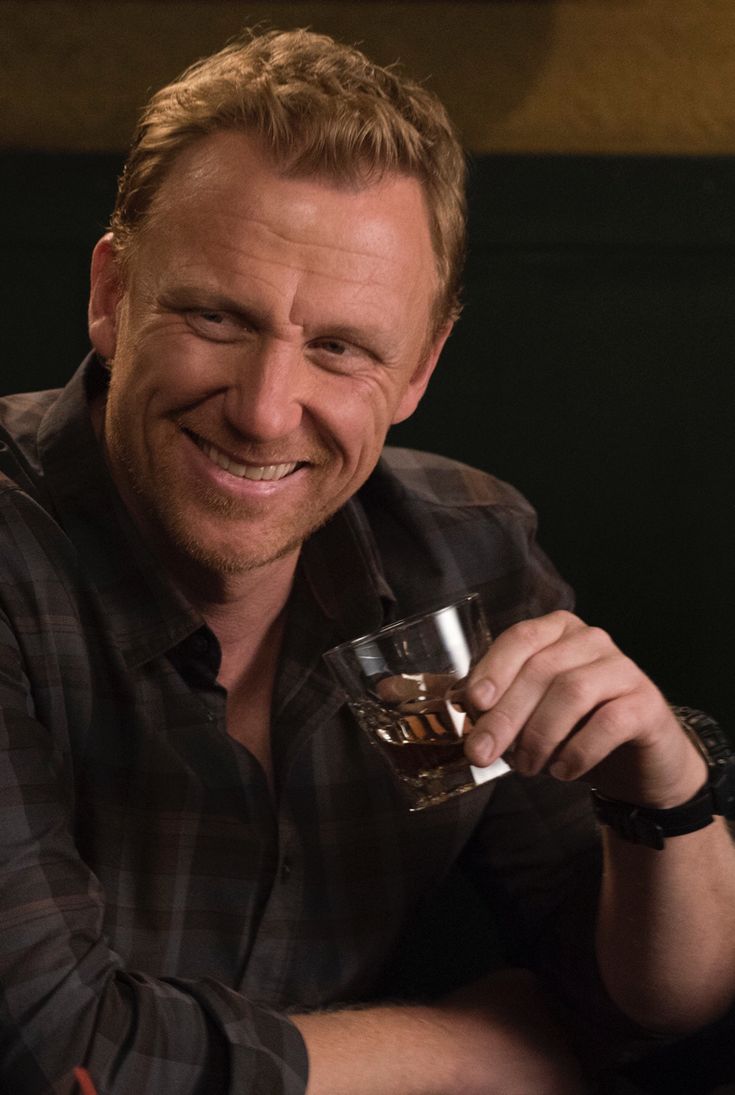 a smiling man holding a glass in his right hand and looking at the camera with an intense look on his face