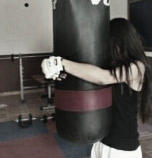 a woman is standing next to a punching bag in a gym with her arms wrapped around the punching bag