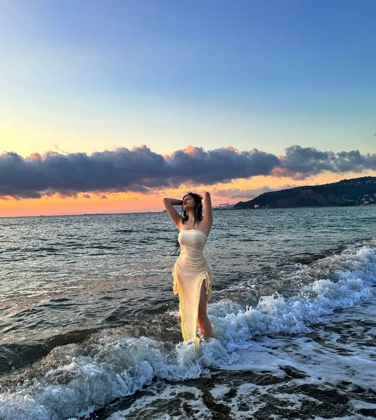 a woman is standing in the water at the beach with her hands up to her head