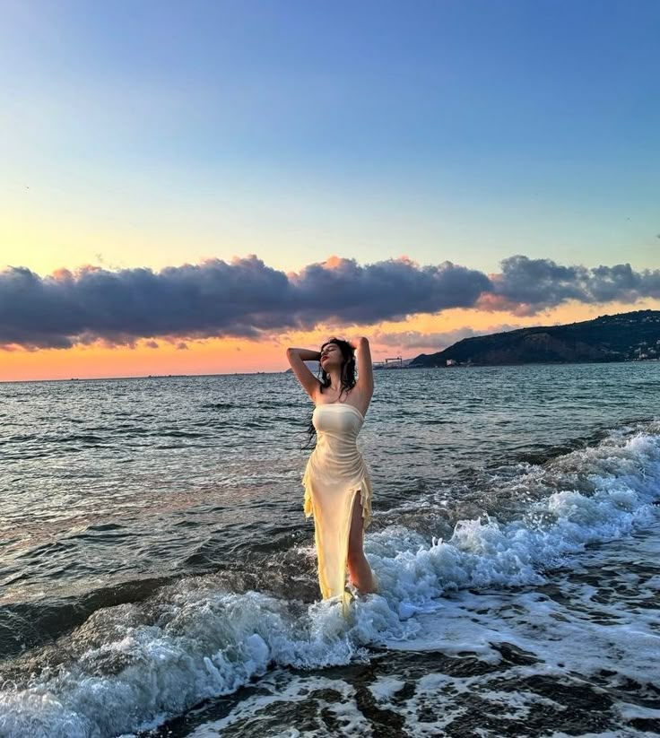 a woman is standing in the water at the beach with her hands up to her head