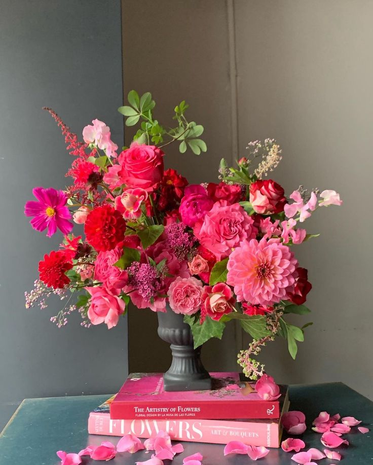 a vase filled with pink and red flowers on top of two books