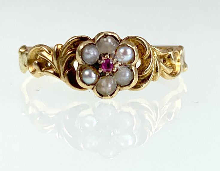 The forget me not was a popular motif during the Victorian Era; jewelry with the design was given as tokens of love and friendship, as well as used in mourning pieces. This wonderful example is crafted in 18 karat yellow gold, with stunning feathered and scrolled repousse work on the shoulders and ring top. Six natural seed pearls form the petals, with a bright pink ruby holding court in the center. It has an open locket back, which probably held a lock of hair at one point in time. Delicate and feminine, it is a true treasure from days gone by! Details (approximate) Size (can be resized): 6.5 Weight: 1.4 grams Materials: Gold, Ruby, Pearl Metal: 18K yellow gold Marks: None Condition: Excellent Antique condition commensurate with age and wear Forget Me Not Ring Gold, Victorian Rings Antique, Victorian Era Jewelry, Forget Me Not Ring, Open Locket, Antique Jewelry Victorian, Georgian Ring, Lock Of Hair, Pink Ruby