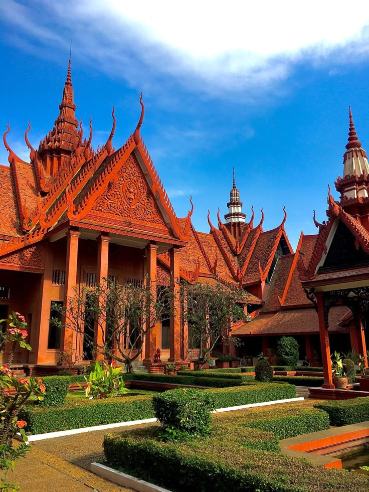 an elaborately designed building with red roofing and ornate garden beds in front of it