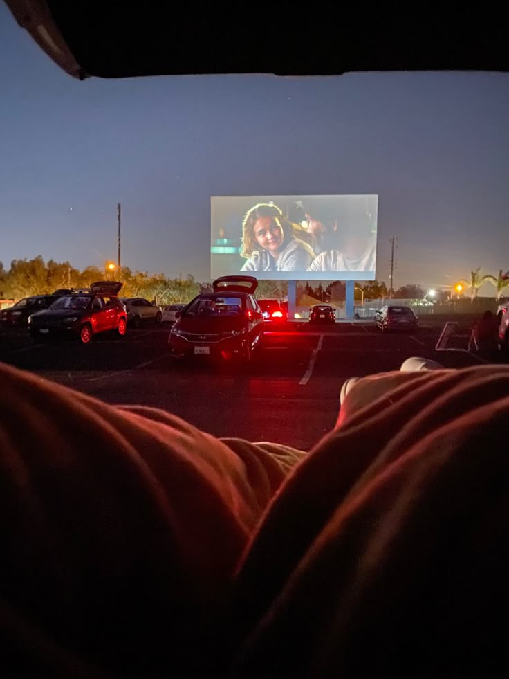 people watching a movie in a parking lot at night with cars parked on the side