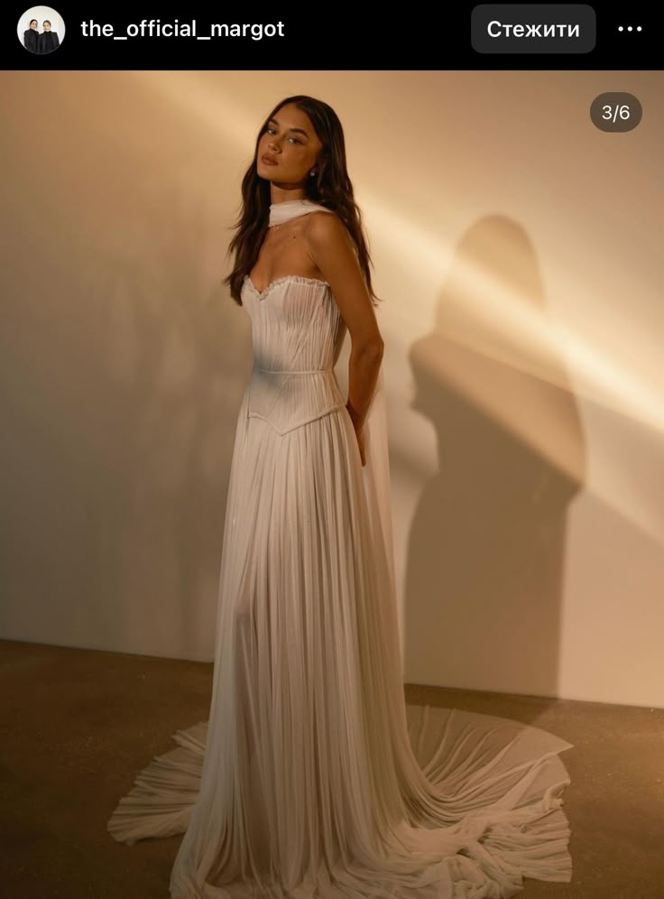 a woman in a white dress is posing for a photo with her shadow on the wall behind her