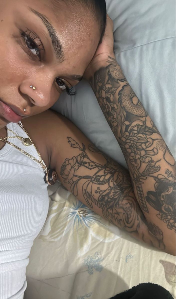 a woman laying on top of a bed next to a pillow with tattoos on her arm