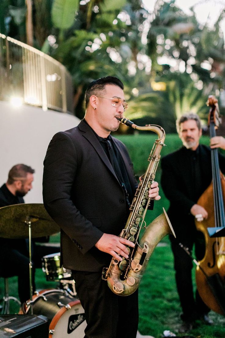 two men in suits are playing instruments on the grass while another man stands behind them