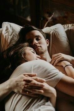 a man and woman laying in bed with their arms around each other as they cuddle