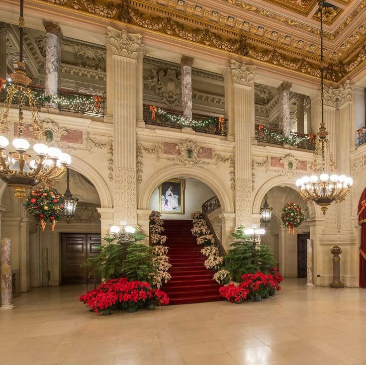 an ornately decorated lobby with chandeliers and red carpeted stairs leading up to the first floor