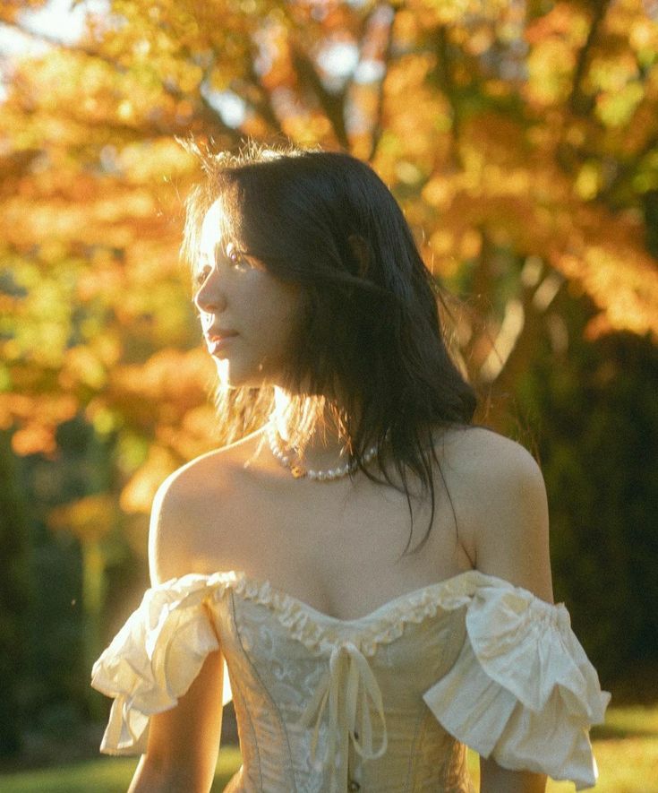 a woman in a white corset standing on grass with trees in the background