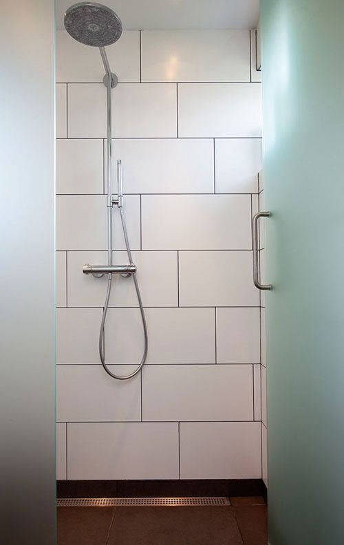 a walk in shower sitting next to a white tiled wall and floor with a hand held shower head