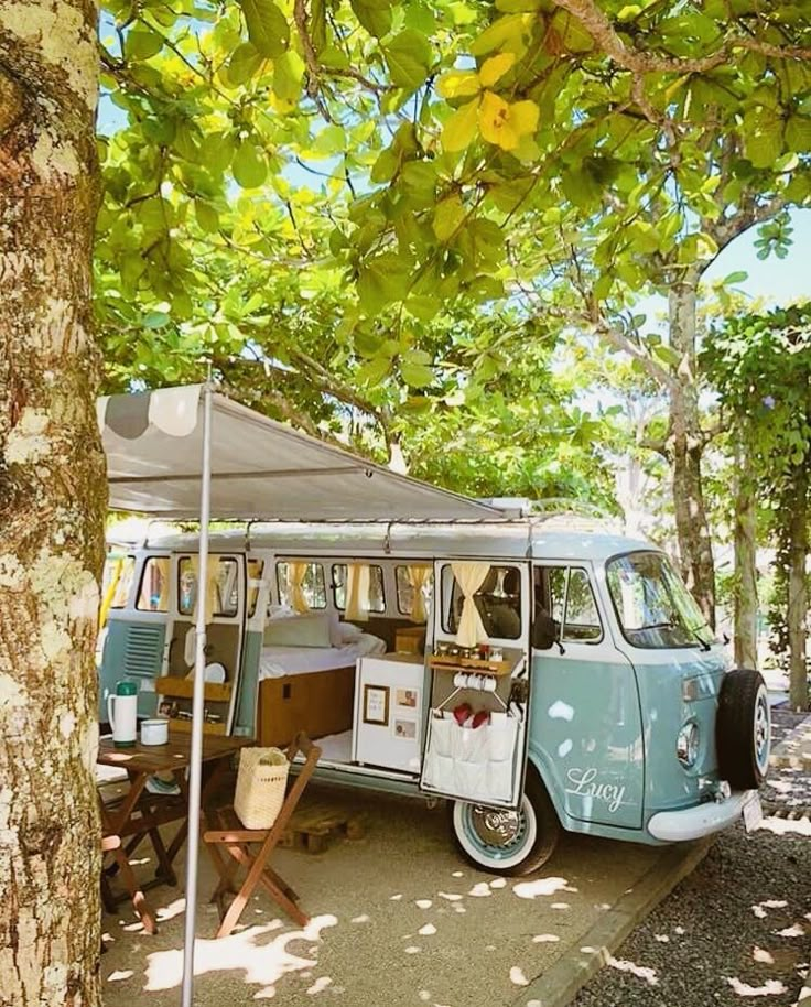 an old vw bus is parked under a tree in the shade with its awning open