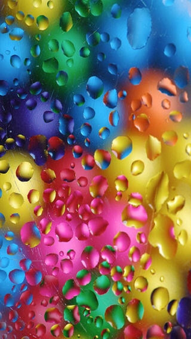 colorful drops of water on the surface of a rainbow colored glass window with multicolored bubbles