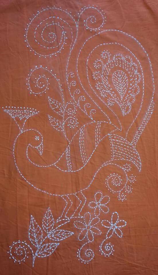 an orange table cloth with white embroidery on it and flowers in the center, sitting on a wooden surface