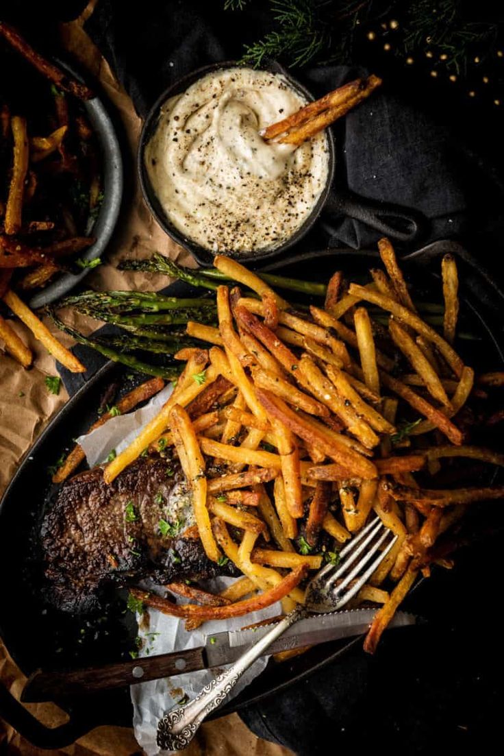 a plate with french fries, steak and dipping sauce on it next to a bowl of mashed potatoes