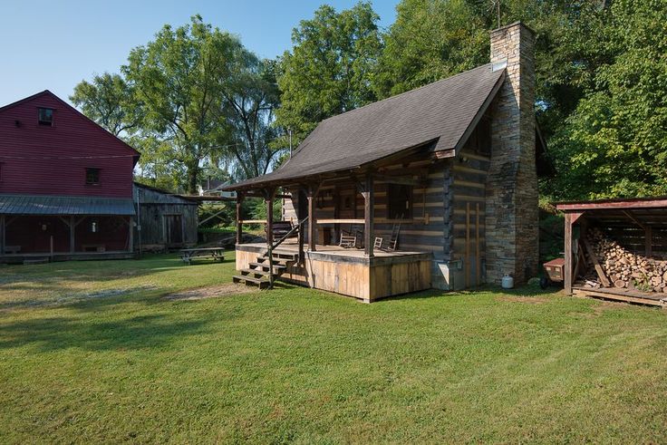 an old log cabin sits in the middle of a grassy field next to a red barn