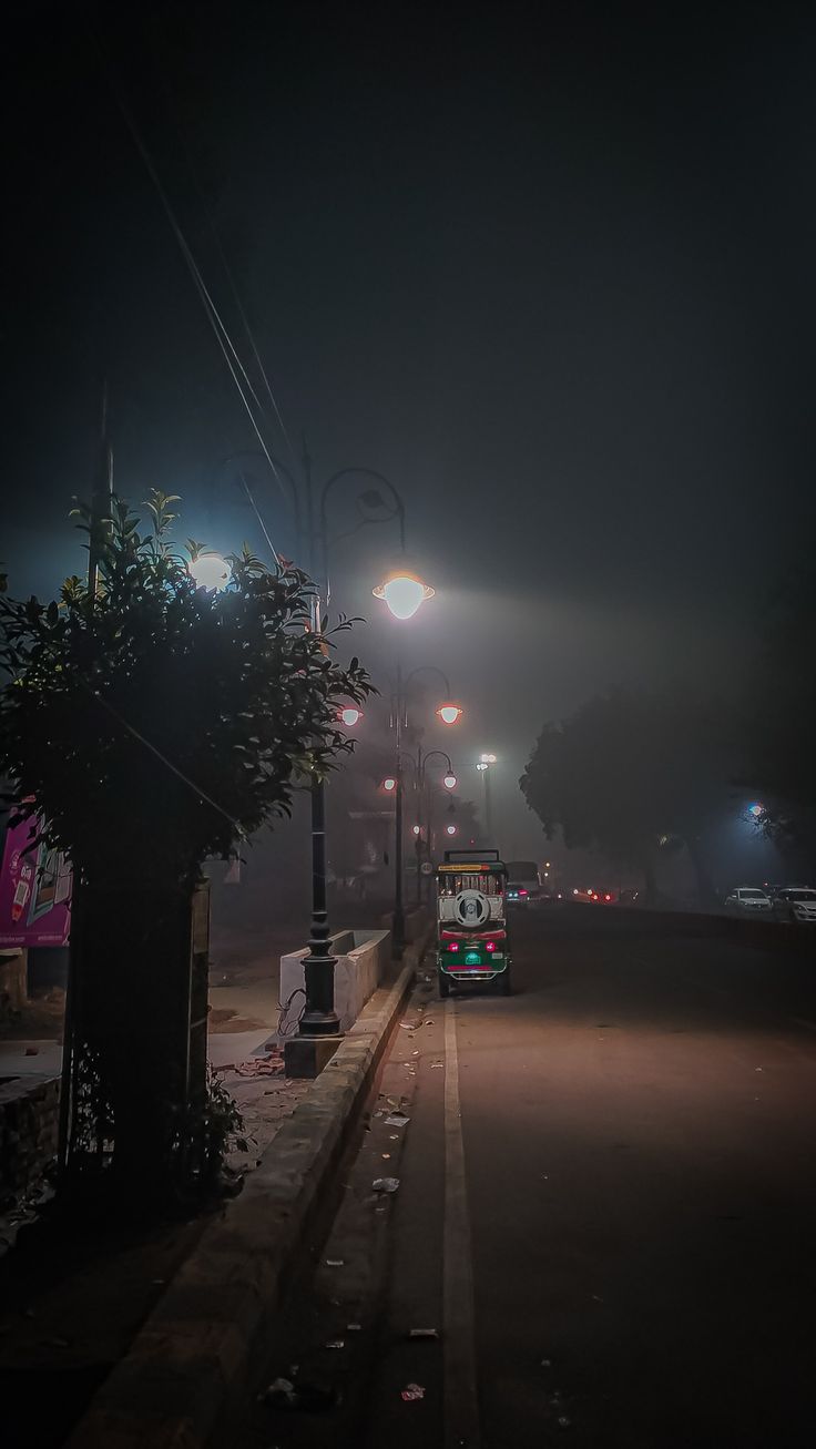 a bus is driving down the street at night with its lights on and fog in the air